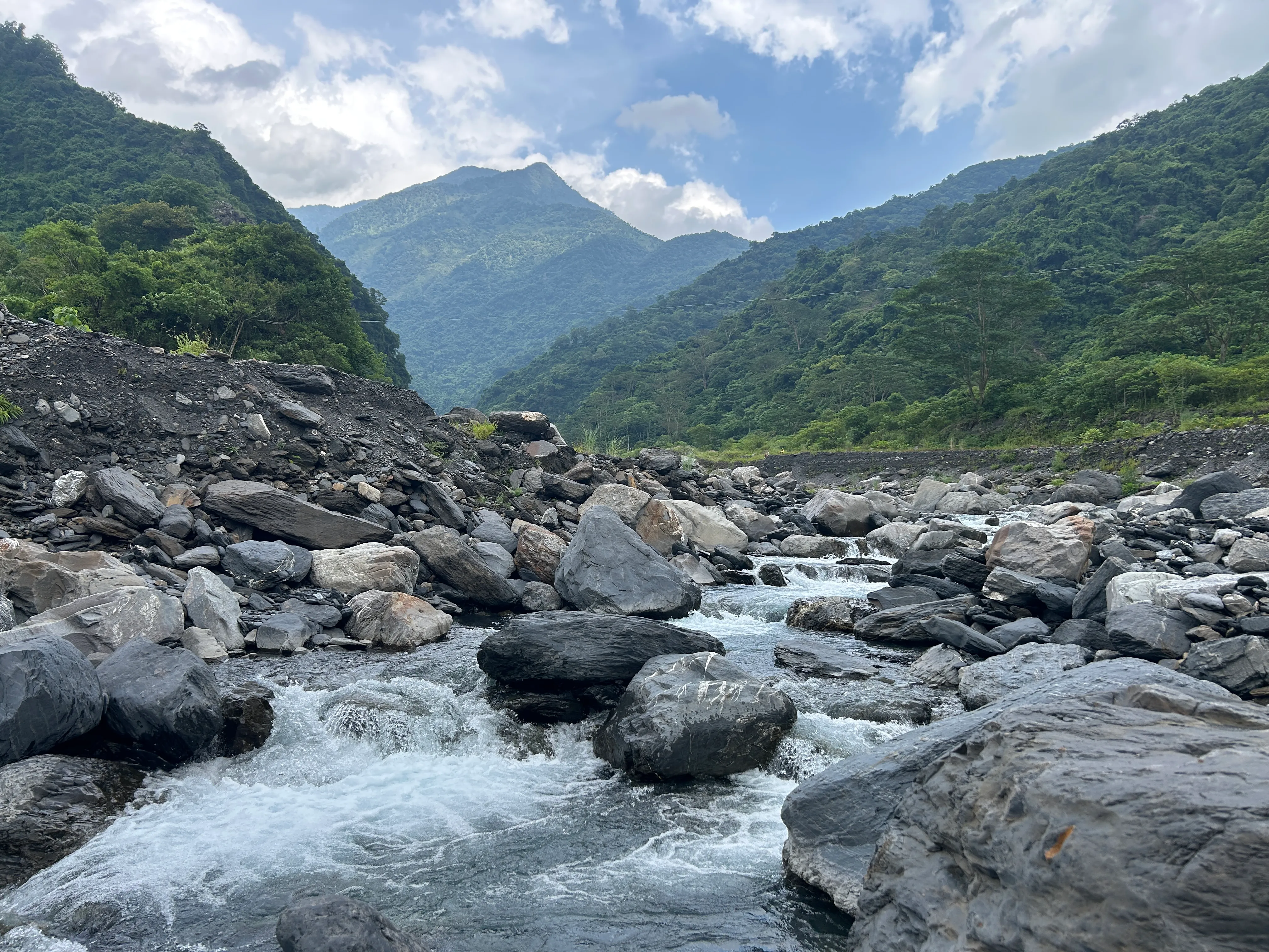 Clear water rushing over boulders in Walusi River, a peak rising beyond