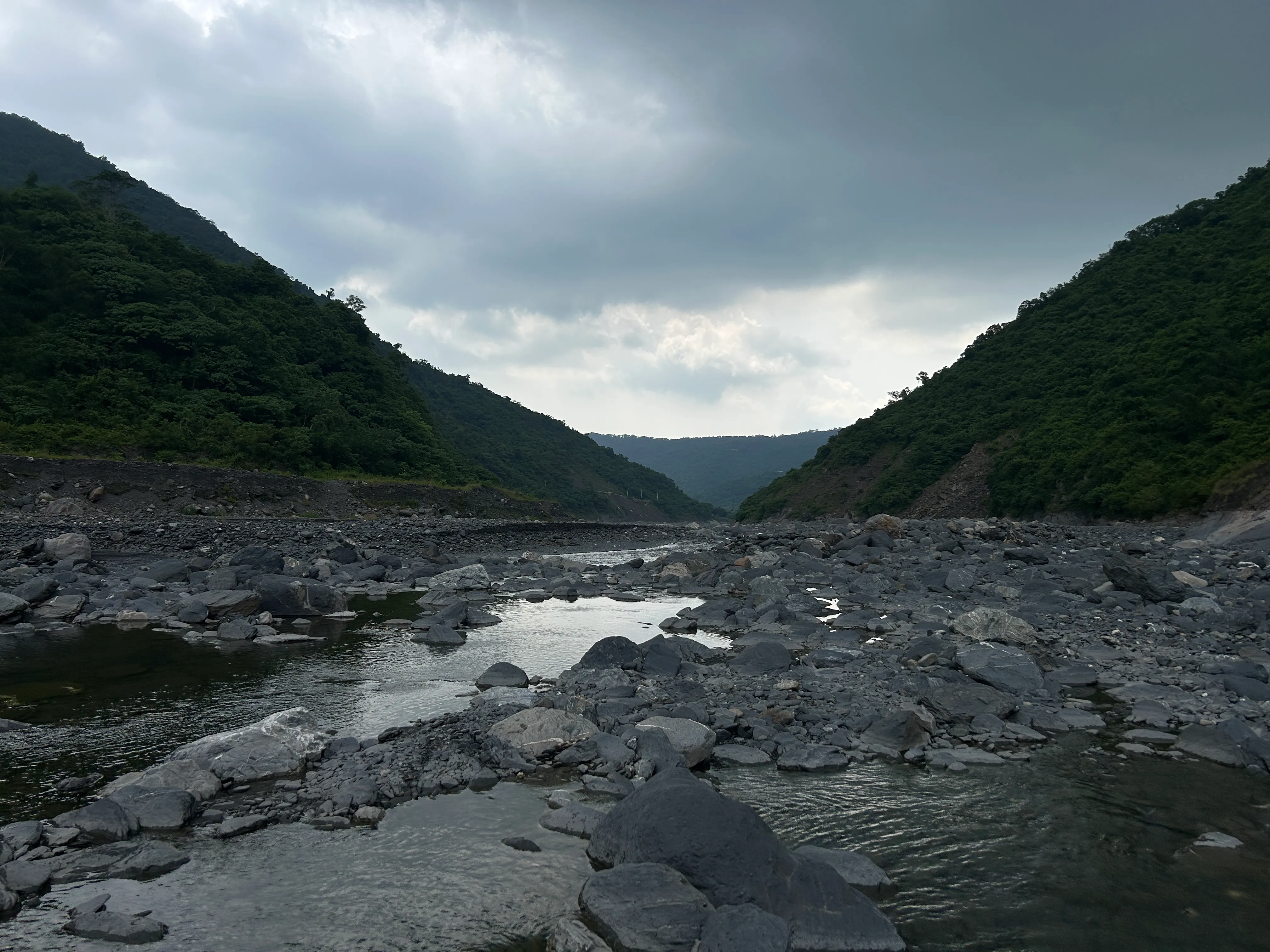 The broad stony riverbed of Walusi River reaching back toward its mountain source under cloud